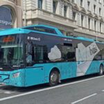 A blue and white Aerobus making a stop on a busy downtown street, facilitating passenger transportation between the airport and the urban core.