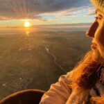 A woman gazes at the sky while traveling in a hot air balloon over Ampurdà. The sun shines brightly and the altitude is evident.