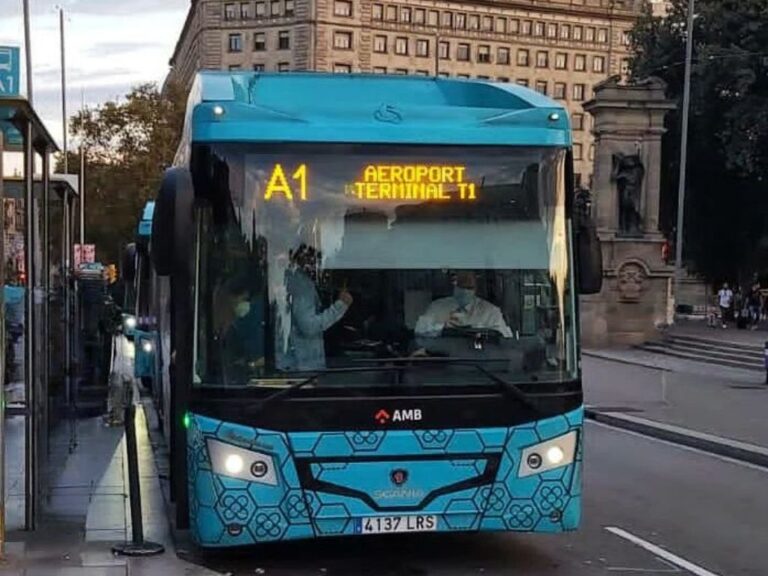 A blue and white Aerobus parked in Plaza Catalunya, with passengers boarding and alighting, in the center of Barcelona, standing out as an important connection point between the airport and the city.
