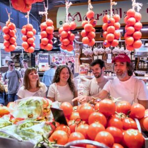 Participants selecting fresh ingredients from La Boqueria market, including ripe tomatoes, succulent seafood, and fragrant herbs.