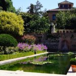 Exterior of the Alhambra Gardens featuring a verdant and lilac space with a pool in the center.
