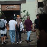 A group of people gather at a café called 'Giovanni' for breakfast. The daylight illuminates their backs.