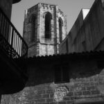 Photograph shows one of the towers of the bell tower of the Barcelona Cathedral peeking out between the buildings of L'Eixample.