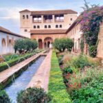 Image in one of the emblematic gardens of the Alhambra where you can observe the construction of a house, a fountain walkway, and vegetation surrounding it.