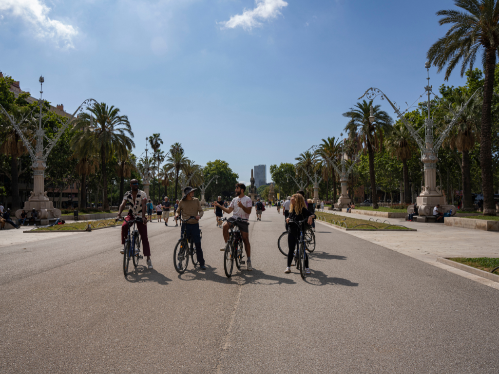 Group of people on electric bikes smiling at the camera near Arc de Triomf on Passeig de Sant Joan, Barcelona.