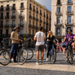 Guide standing and members of the group listening in a plaza in Poble Nou, Barcelona, with bikes.